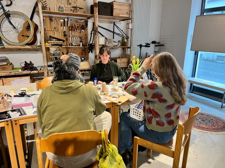 Teilnehmer des Schnuppertags Drei Personen sitzen an einem Tisch und basteln Collagen bzw. Lesezeichen